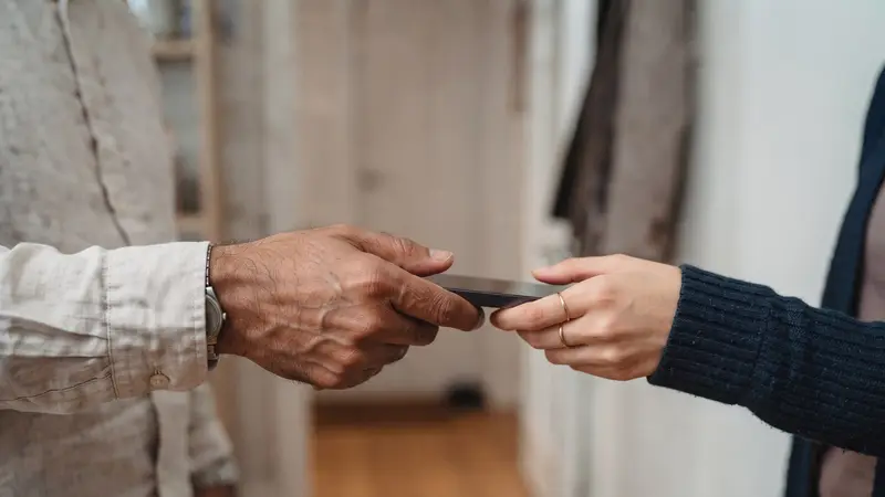 The hand of a father passing a phone to the hand of his daughter in a home hallway, a quiet handover of her marriage profile